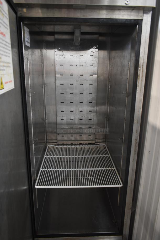 Commercial stainless steel refrigerator interior with wire shelf, used condition, safety label visible on the left panel.