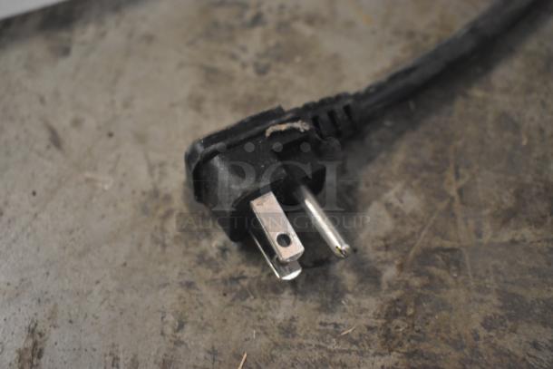 Black three-prong power plug with frayed insulation, showing signs of wear, resting on a concrete surface.