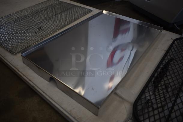 Stainless steel grill tray with mesh cooking grid, minor scuffs, reflective surface, suitable for outdoor cooking.