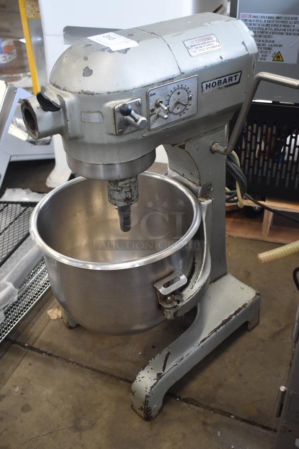Vintage Hobart industrial mixer, model unknown, with stainless steel bowl. Visible wear and rust on body. Functional dials and levers.