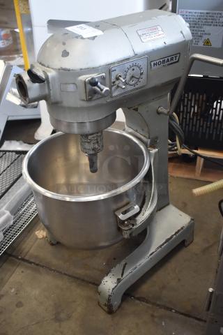 Vintage Hobart industrial mixer, model unknown, with stainless steel bowl. Visible wear and rust on body. Functional dials and levers.