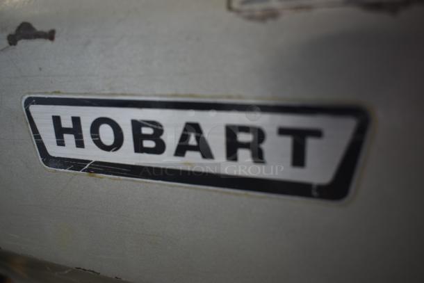 Hobart industrial kitchen equipment label, metallic with black text, minor wear visible, showcasing brand logo.