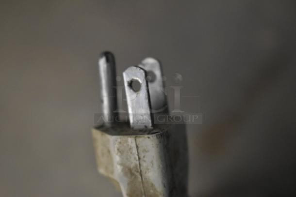 Close-up of a weathered three-prong electrical plug with visible grime and rust on the metal parts, indicating wear.