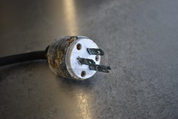 Worn three-prong electrical plug with corrosion and rust, indicating heavy use or age. No visible labels or markings.