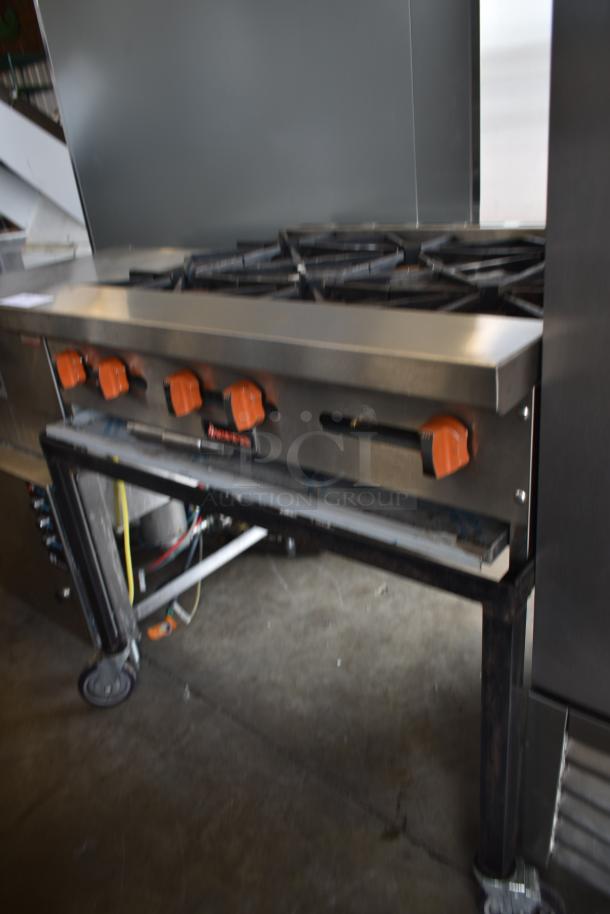 Commercial-grade stainless steel gas stove with six burners, orange knobs, and a sturdy metal frame.