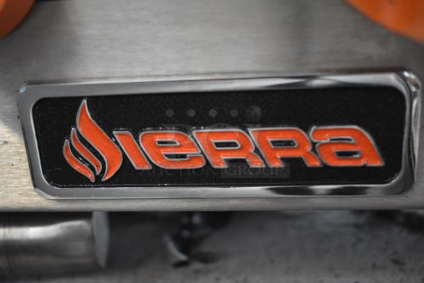 Close-up of a Sierra metal badge with orange lettering and flame icon, set on a black background and silver trim, in excellent condition.