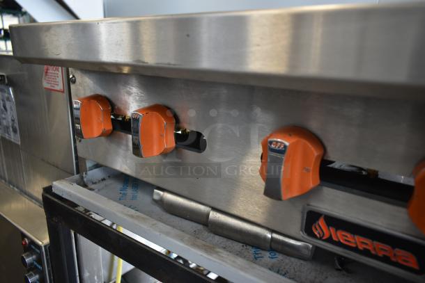 Sierra industrial gas range with three orange control knobs, stainless steel finish, good condition, visible warning labels.
