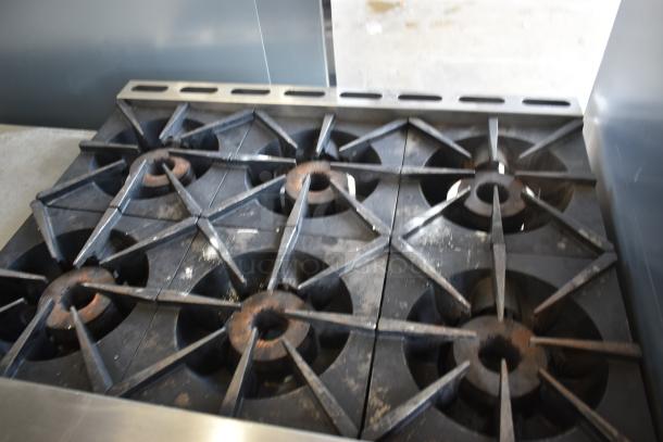 Commercial six-burner gas stove with cast iron grates, showing signs of wear, ideal for restaurant use.