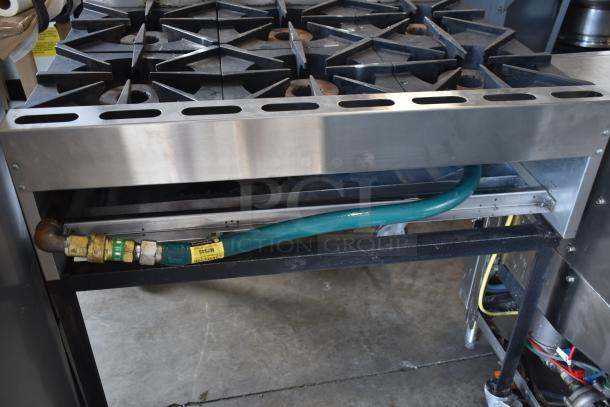 Commercial stove with six-burner cast iron range, stainless steel body, and connected green gas hose. Used condition.