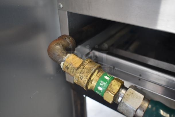 Brass gas valve with flow markings and patina, connected to metal piping in a commercial setting, showing some wear.