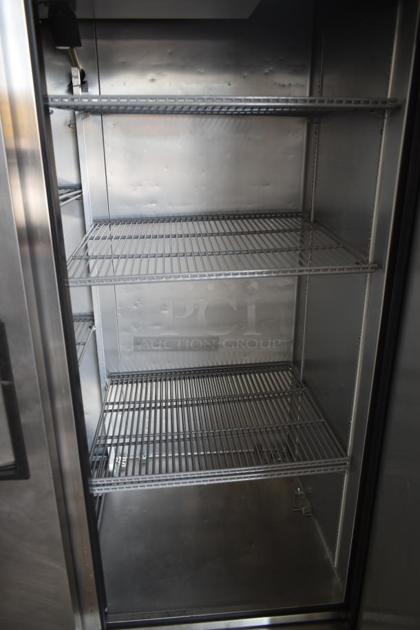 Commercial stainless steel refrigerator interior with four wire shelves. Clean, minor wear visible. Ideal for restaurant use.