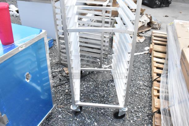 Metal restaurant rack with multiple shelves, on wheels, in used condition. Blue equipment panel and pallets visible nearby.