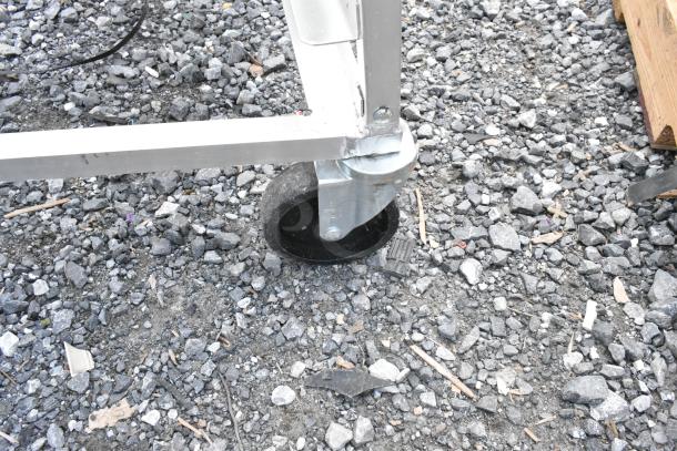 Metal frame with a swivel caster wheel on a gravel surface, showing light wear, suitable for mobile structures or equipment.