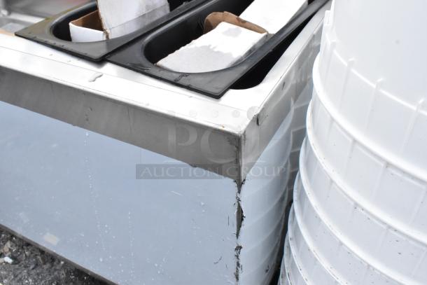 Stainless steel kitchen equipment with visible edge wear and water stains, alongside white plastic storage bins.