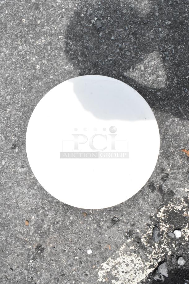Flat white ceramic disc on asphalt surface, showing shadow and slight wear. No visible labels or markings.