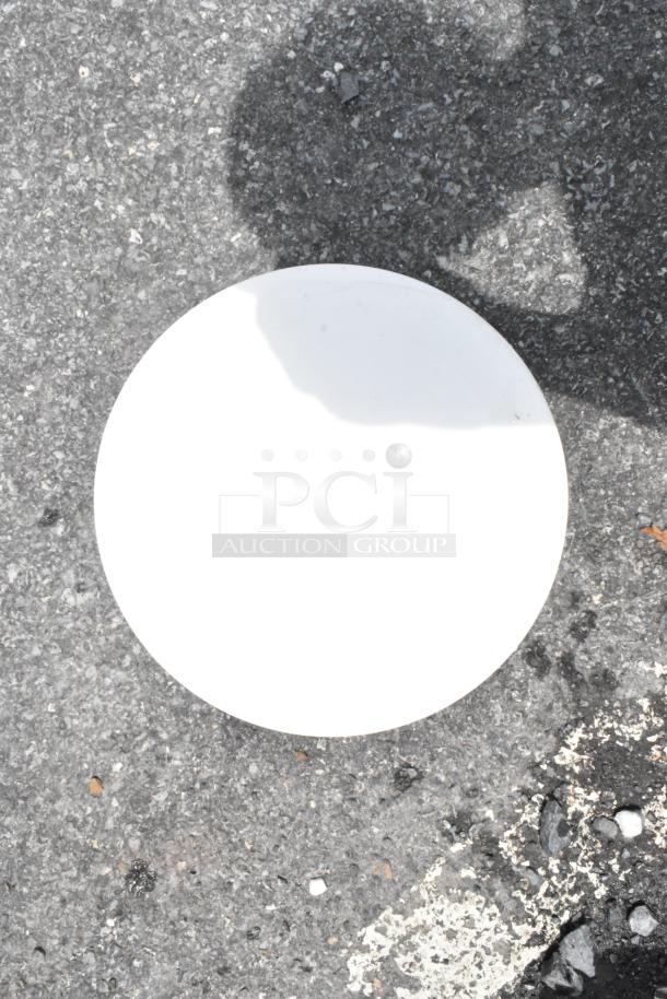 White circular disc on asphalt, likely unmarked frisbee or platter. Shadow partially covers surface. Appears in good condition.