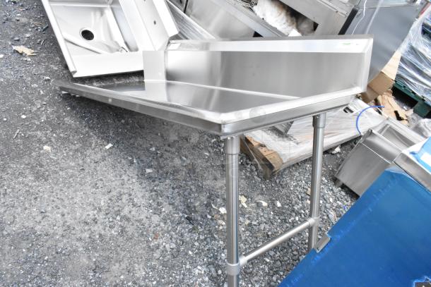 Stainless steel corner prep table, excellent condition, with a backsplash and sturdy tubular legs. Ideal for commercial kitchens.