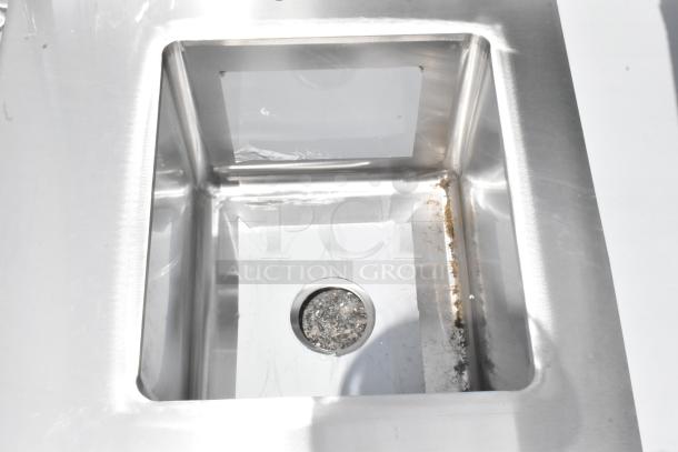 Stainless steel sink with a drain, showing some residue and minor wear. Ideal for kitchen or utility use.