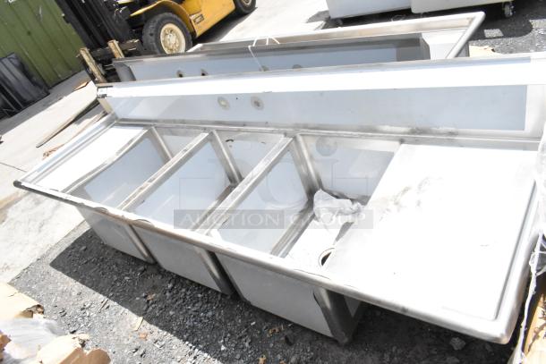 Stainless steel commercial sink with four compartments, used condition, visible surface marks. Ideal for kitchen use.