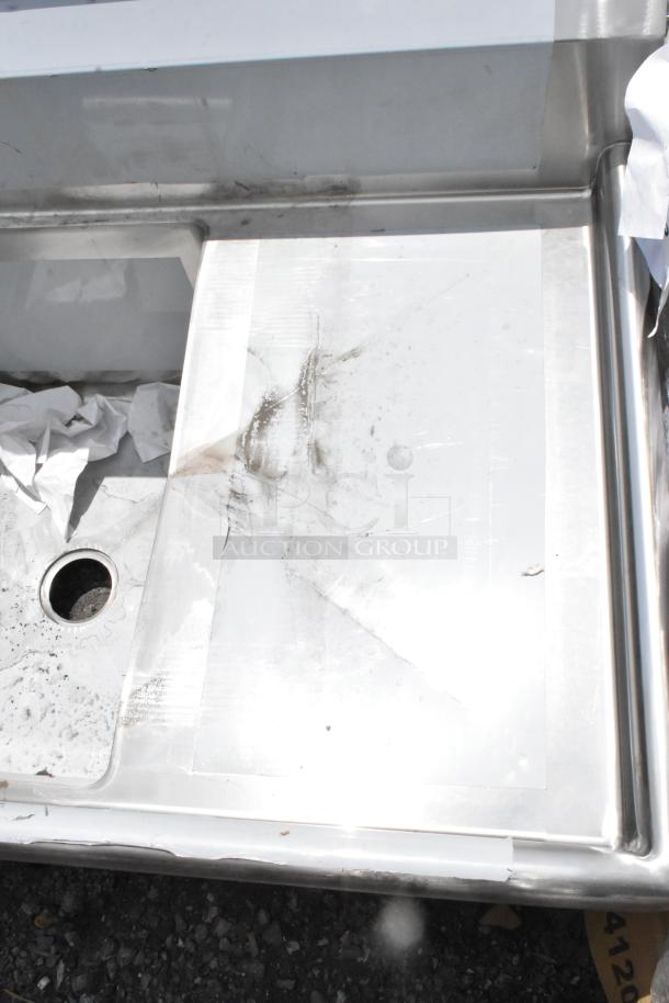 Stainless steel sink with integrated drain, surface wear and smudges visible; includes paperwork and packaging debris.