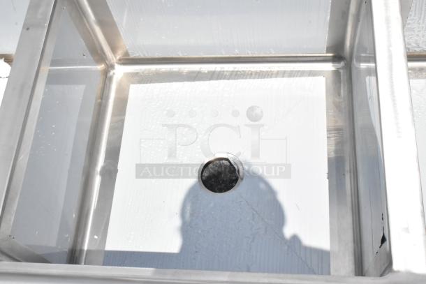 Stainless steel industrial sink with visible drain hole, in excellent condition, reflecting light.