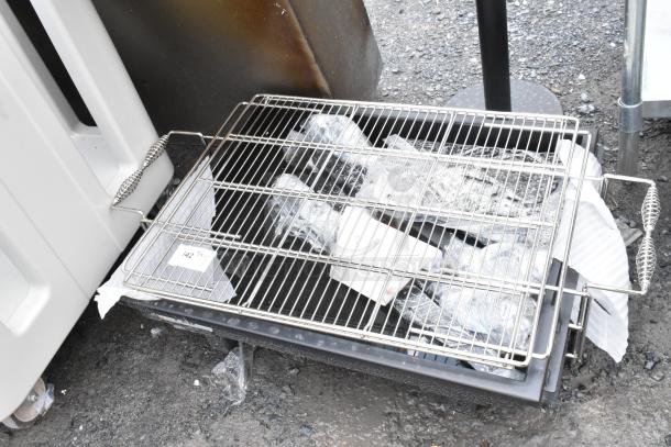 Metal grill rack with side handles, resting on a bin with plastic bottles. Label indicates "142". Good condition.