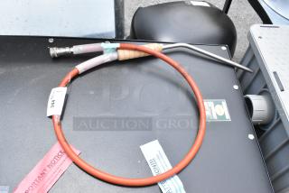 Red industrial hose with metal fitting and handle, labeled "344," set on a dark surface. Notices and tag details visible.