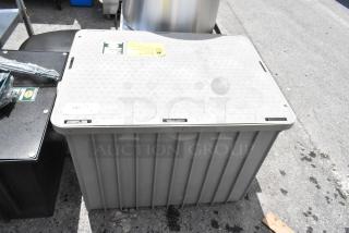 Large gray plastic storage container with textured lid and visible stickers. Condition shows outdoor usage.