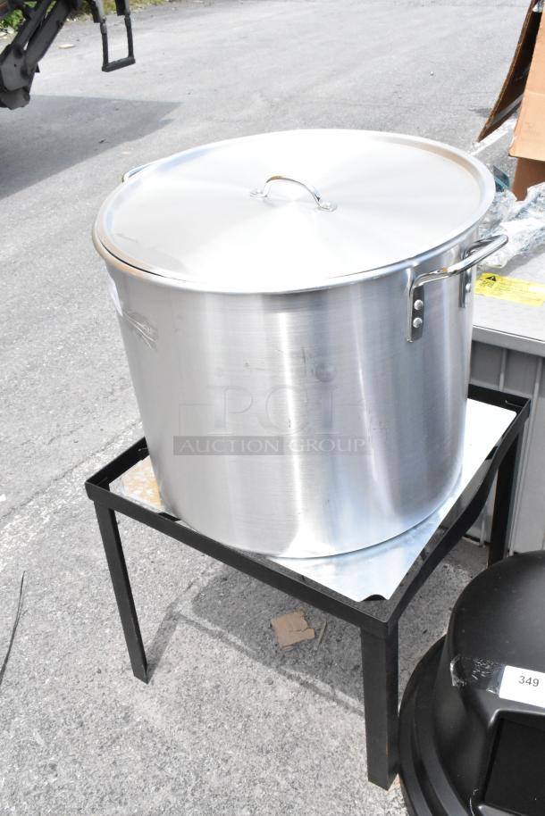 Large stainless steel stock pot with lid on a black metal stand, in good condition. Ideal for high-capacity cooking.