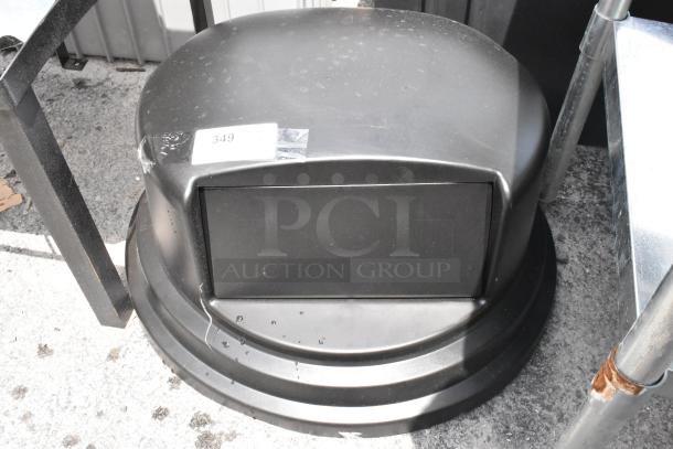 Black outdoor trash can with a domed lid, visible scuff marks, and a label numbered "349". Features swing door and sturdy base.