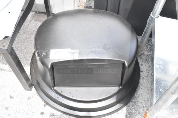Black plastic waste bin lid with flapper door, slightly scuffed, auction tag "349" affixed on top.