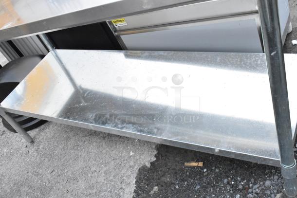 Stainless steel utility cart with two shelves, sturdy frame, minor surface scratches, caution sign visible on top.