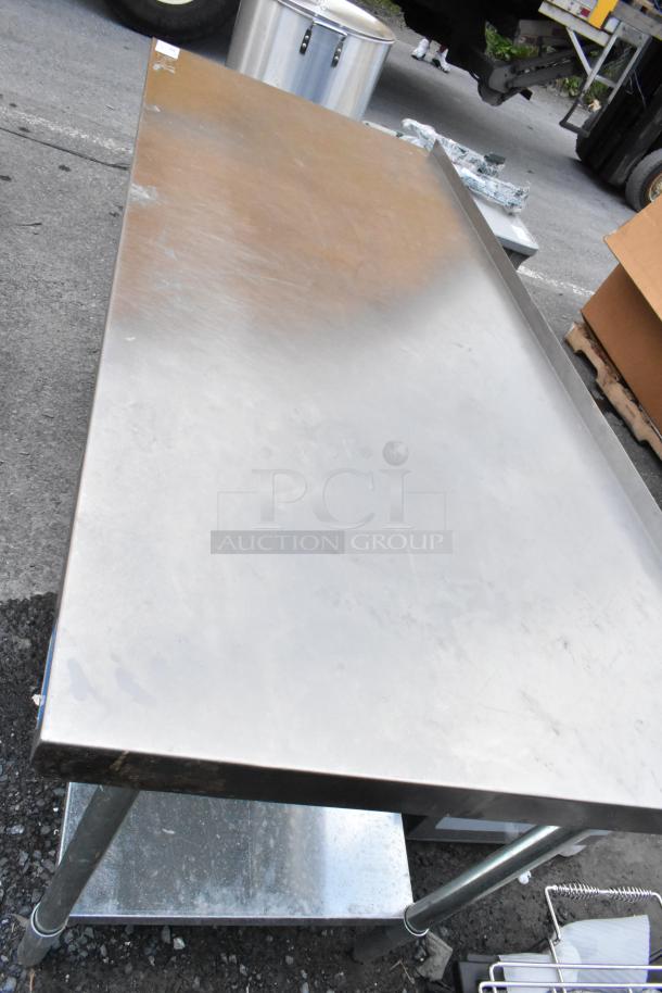 Stainless steel work table with lower shelf, industrial-grade, used condition, scuff marks visible on surface.