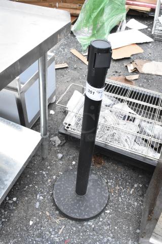 Black retractable stanchion post with a round base, label reading "351", in used condition, outdoor setting.