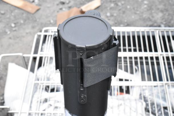 Black cylindrical device with a black strap, likely a holder, in good condition. Mounted on a metal rack.