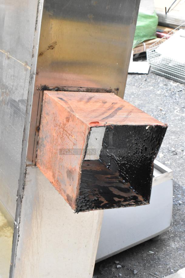 Rusty industrial metal chute with black interior, attached to a larger metal structure, showing signs of wear.