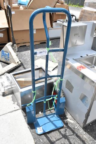 Blue hand truck with solid wheels, visible wear, and load capacity label "353." Tied with green straps.