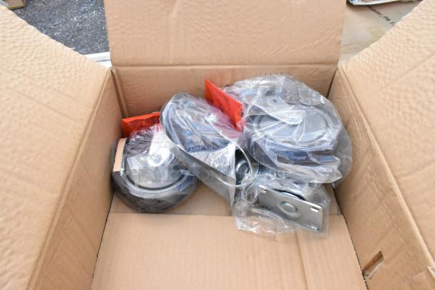Box of new caster wheels, sealed in plastic, various sizes, metal base plates. Tags indicating model numbers visible.