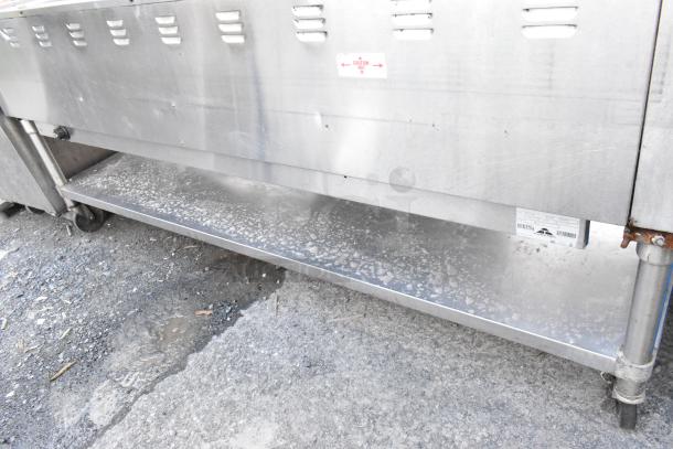 Commercial stainless steel warming cabinet with vented doors, caution label, and lower shelf, showing signs of wear.