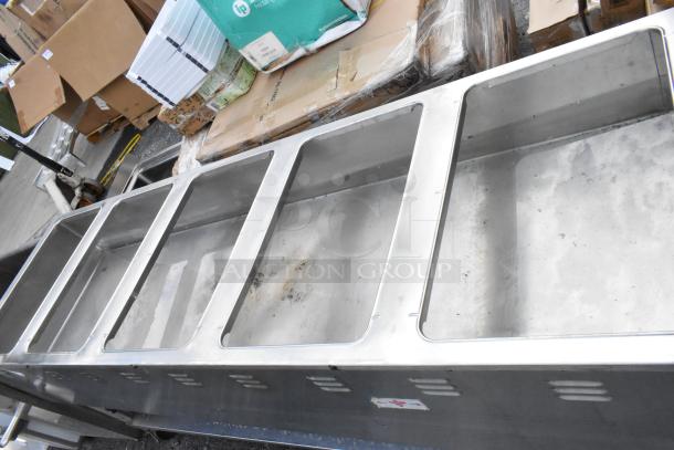 Stainless steel commercial sink with five deep compartments, visible wear and markings, suitable for industrial kitchen use.