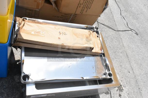 Stainless steel tray with dented corners and cardboard packaging marked "512" on top, placed on a concrete surface.