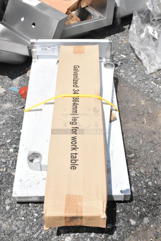 Cardboard box labeled "Galvanized 34-inch leg for work table" with metal brackets on gravel. Item tag present.