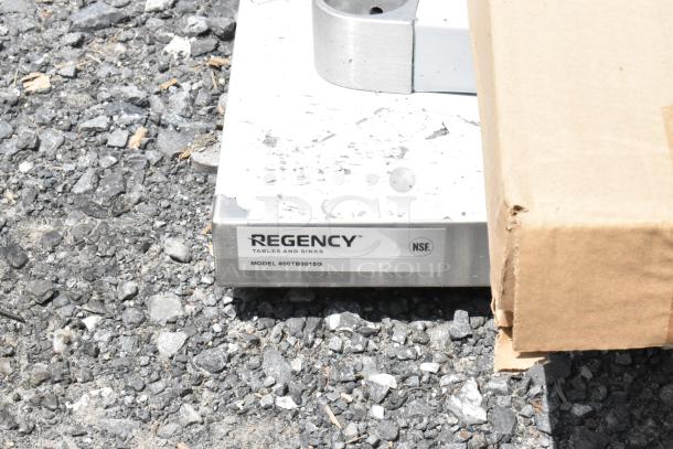 Regency stainless steel table base, Model 600TB3015G, NSF certified, on gravel surface. Condition: lightly worn.