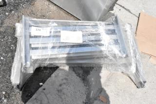 Stacked stainless steel grates wrapped in plastic; visible tags indicate a quantity of one, auction details, and a lot number "370".
