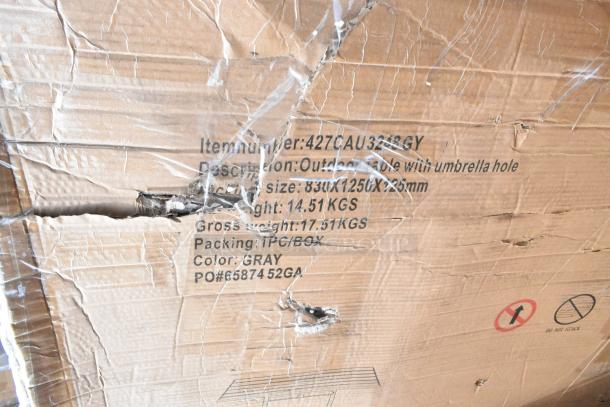 Damaged cardboard box labeled "Outdoor Table with umbrella hole," dimensions 83x125x75cm, color gray, item number 427CAU3218GY.