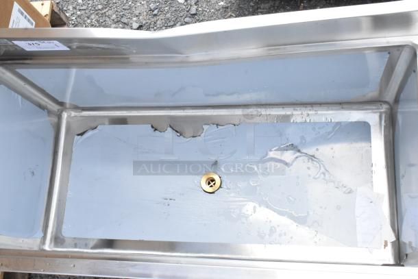 Stainless steel sink with a central drain, some surface scratches and signs of wear, includes attached adhesive label indicating product details.