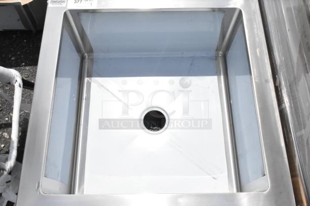 Stainless steel commercial sink with a square basin and central drain, marked "Steelon" and "377" indicating model and lot.
