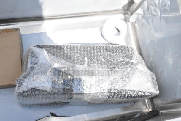Bubble-wrapped rectangular item in new condition, placed on metal surface, next to a cardboard box and foam ring.