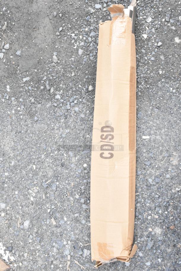Cardboard box on gravel marked "CD/SD," slightly damaged, revealing a metal item inside.
