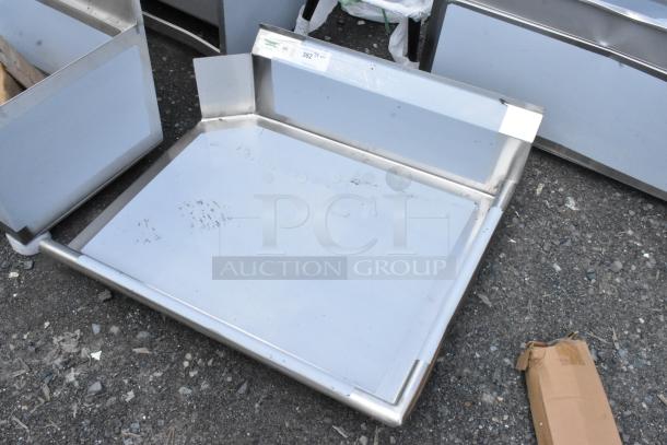 Stainless steel tray with raised edges and label, slightly worn, on gravel surface; ideal for industrial use.